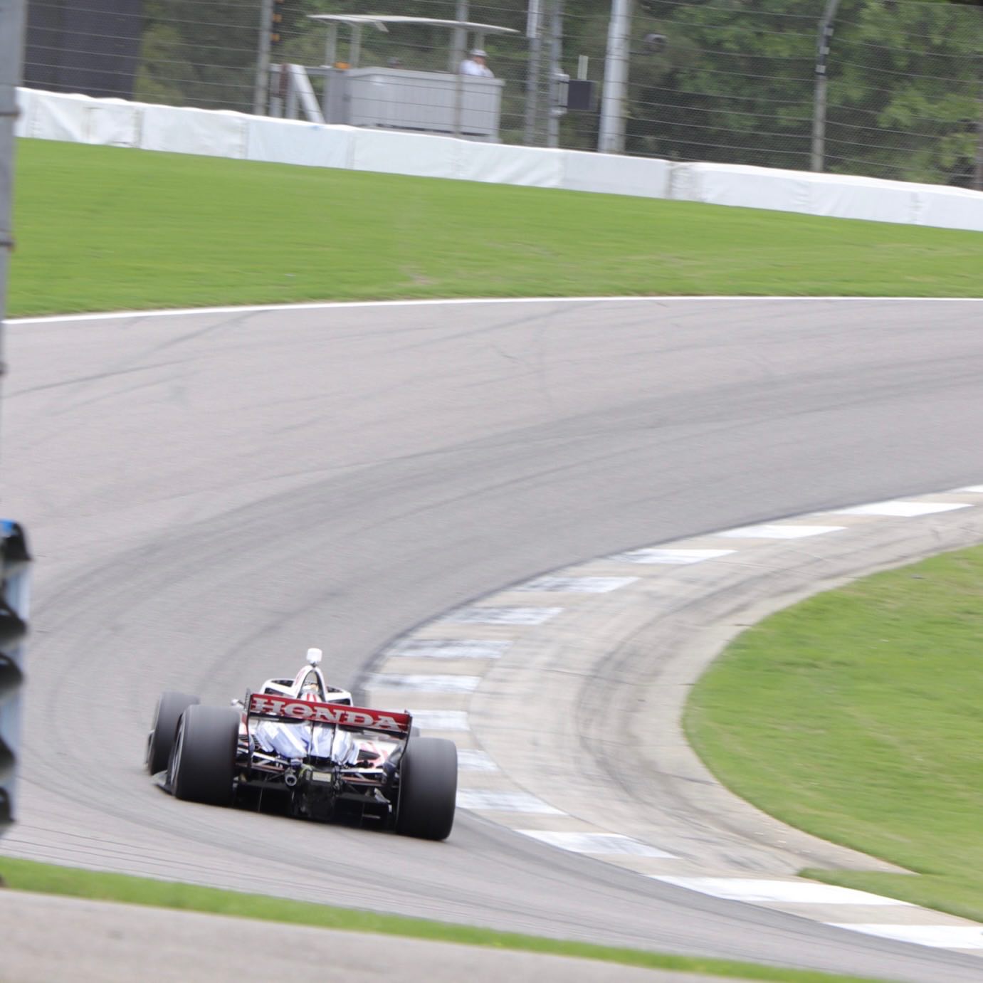 A modern DW12 Indy car from the rear going up a hill at Barber Motorsports Park. The back of the rear wing has the old-school Honda logotype.